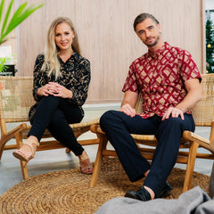 A man and a woman elegantly pose in a workplace environment, both sporting authentic batik shirts, adding a touch of cultural charm to their professional attire