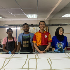 Malaysian artisans proudly posing for a photo with their meticulously handcrafted batik laid out in front of them, showcasing the beauty and craftsmanship of their work