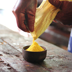 A captivating photo capturing an artisan in the act of pouring yellow batik dye powder pigment into a bowl, showcasing the artistry and precision in the batik-making process