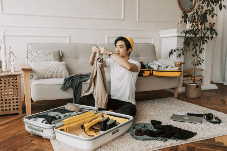 asian man rolling his clothes and putting them into a suitcase