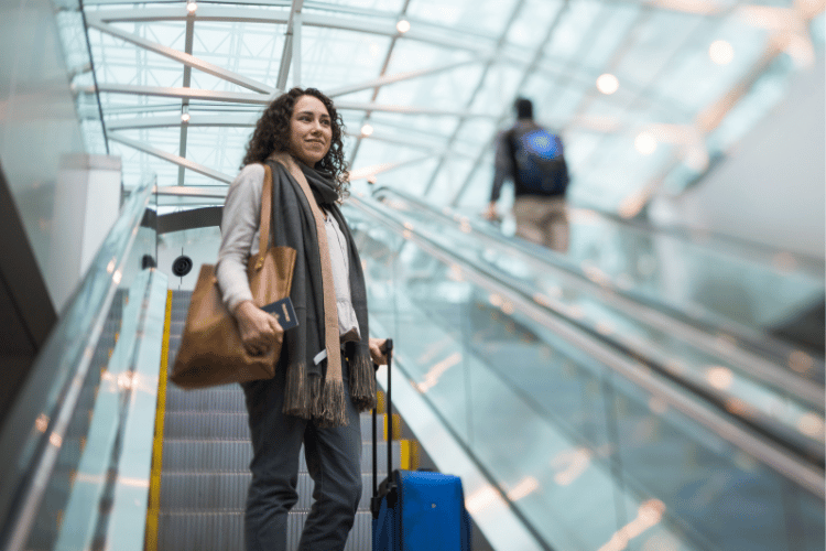 woman wearing a bulky scarf holding a handbag on one shoulder and a suitcase in her other hand