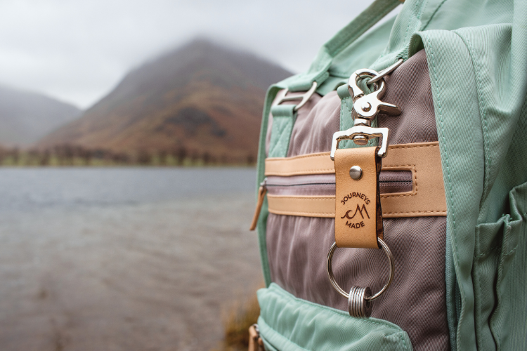 Natural leather travel keychain on a mint green and grey backpack with a mountain in the background
