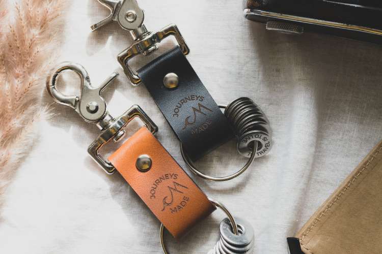 Tan leather keyring and black leather travel keychain with engraved tokens to represent destinations, the perfect travel souvenir and keepsake