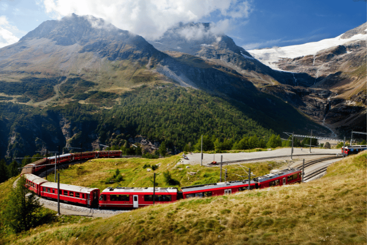 Red train in Switzerland going around a bend with the landscape in the background, part of Europe's best train journeys travel blog