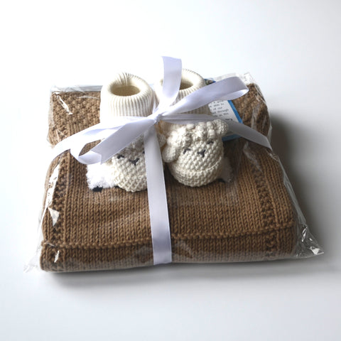 Newborn booties tied under a ribbon on top of a baby blanket.