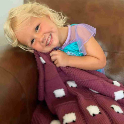 Little girl snuggling with a raspberry coulis blanket, an example of great baby shower gifts from Sheep Dreamzzz