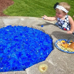 Baby standing beside a firepit filled with blue glass chips