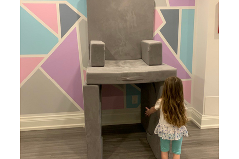 little girl builds a chair that is very tall in the air out of her play couch
