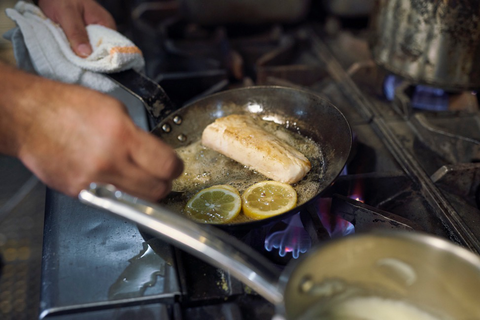 A chef pan-fries a cobia fillet with lemons and olive oil 
