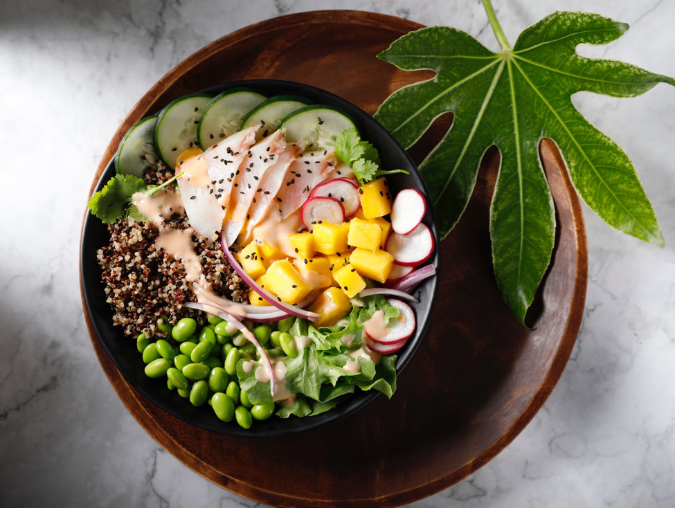 A black bowl filled with slices of Cobia fish, quinoa, cucumber, radishes, and mango