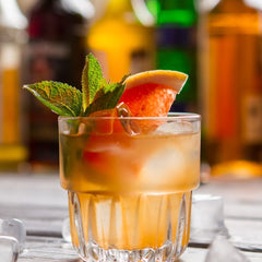 Orange grapefruit herbal tea in short glass with ice, grapefruit slice, and mint