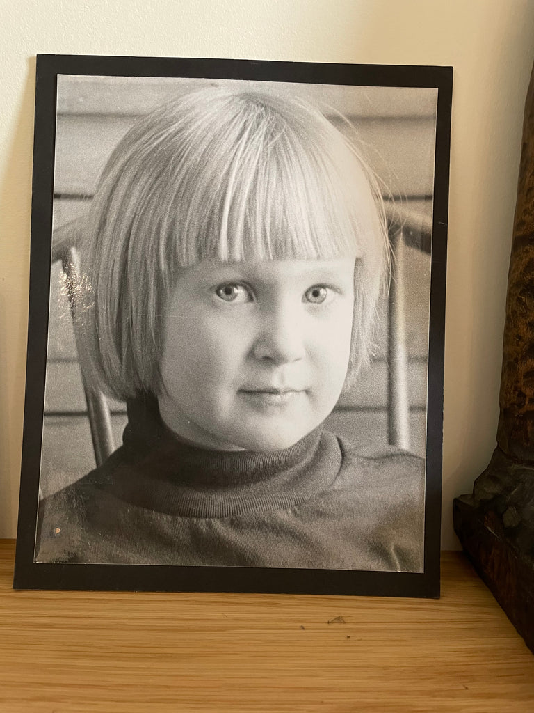 black and white image of a very young little blonde girl, giving a side glance and wearing a dark turtleneck