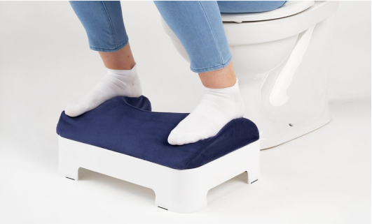 Model sitting on toilet with feet resting on a clean footstool.