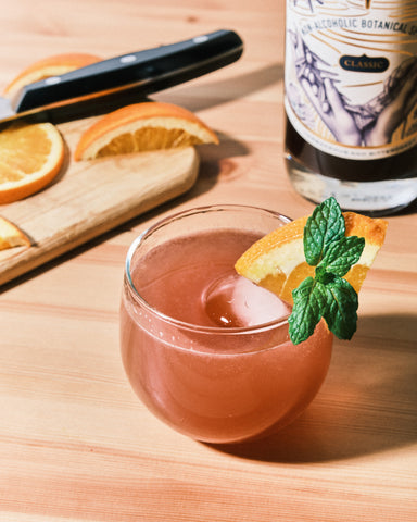 Beverage made with Melati- Nonalcoholic Botanical Aperitif next to orange wedges and a bottle of Melati