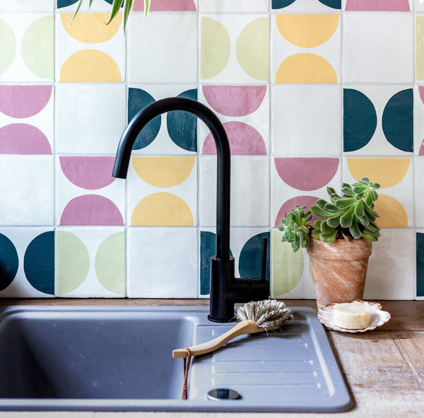 Pink, yellow and blue tiles behind a large ceramic sink and wooden counter