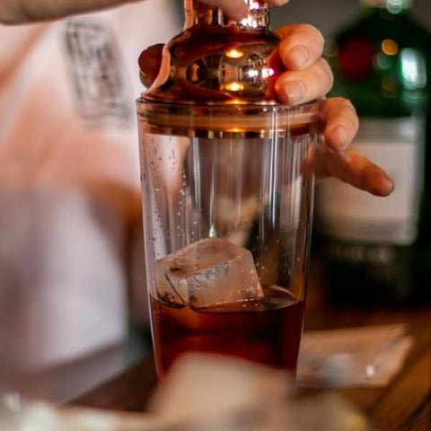 Copper lid glass cocktail shaker with cold brew negroni mix with a cube of ice