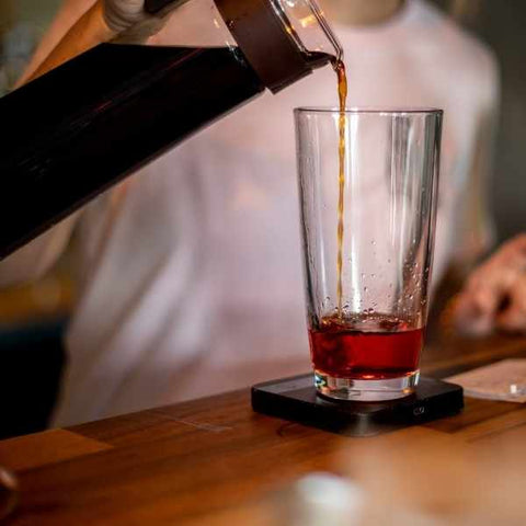 Cold brew coffee in a Mizudashi being poured into a glass cocktail shaker ontop of a luna scale 
