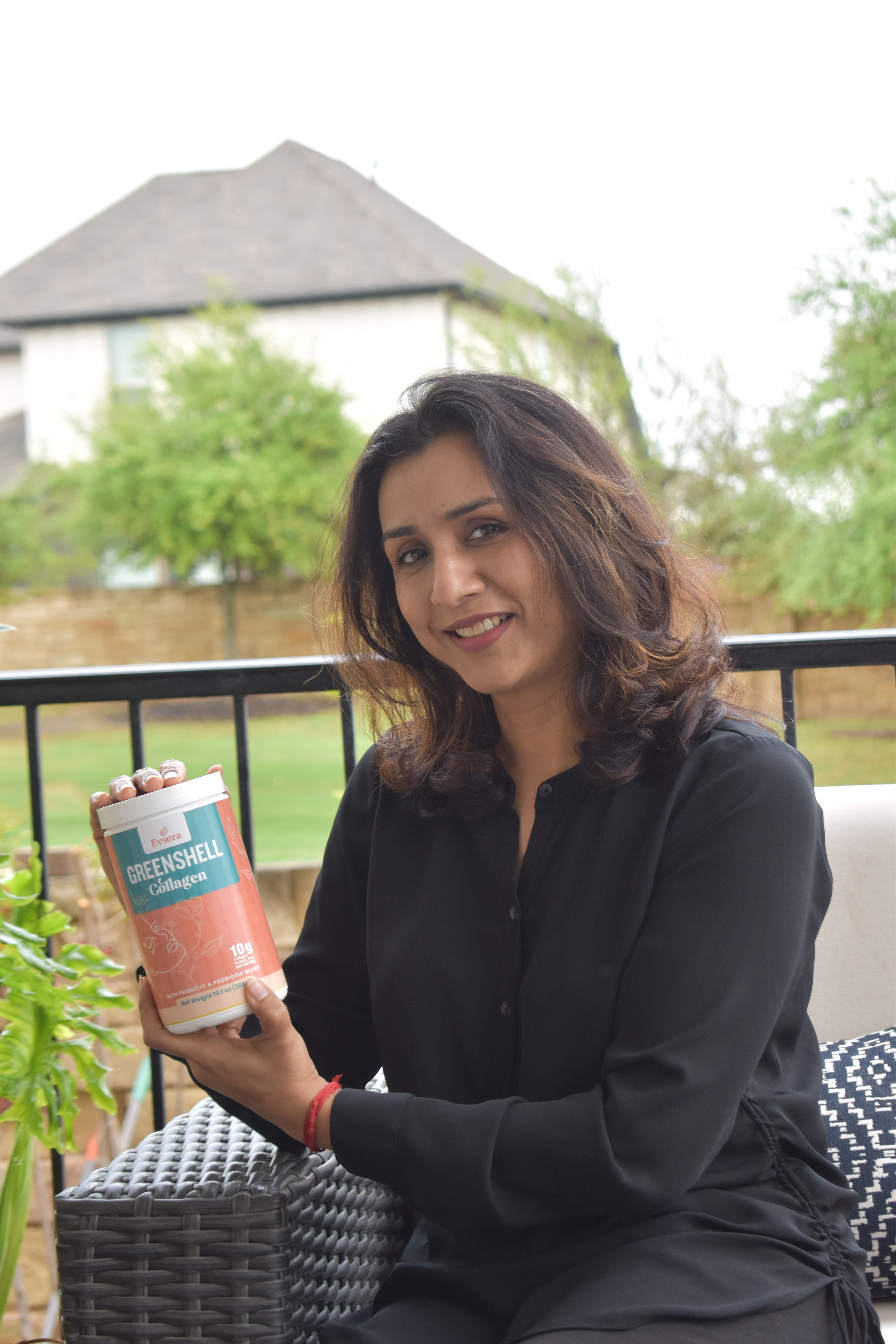 Smiling woman sitting outdoors holding a canister of greenshell collagen.