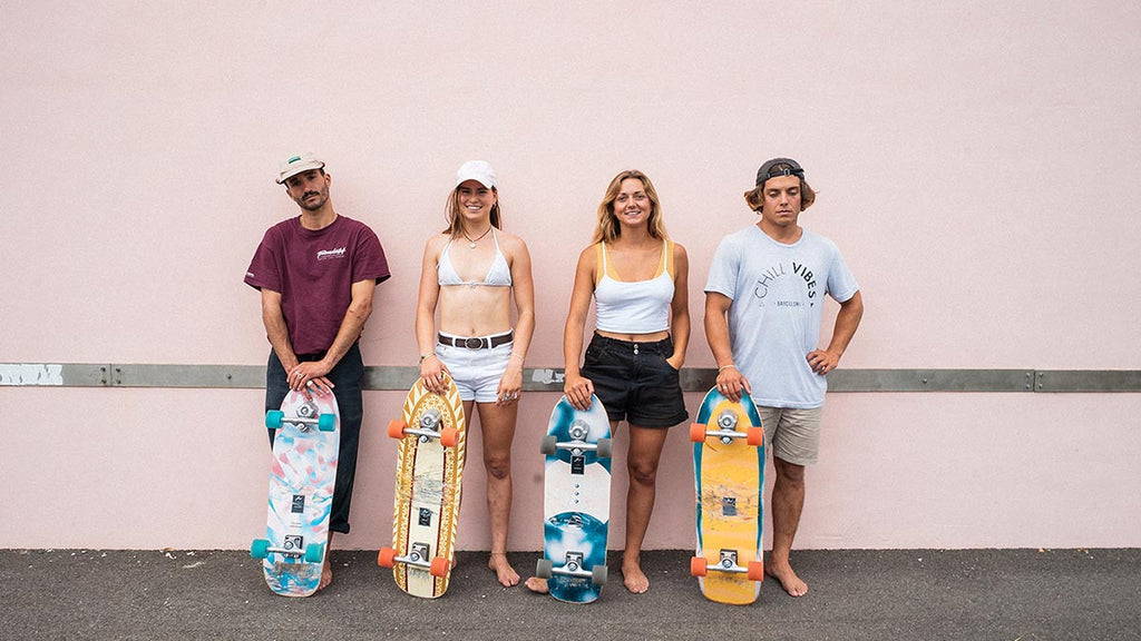 Yow surfskate team standing against pink wall holding surf skates