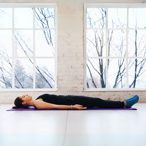 Corpse Pose (Savasana). The image depicts a person lying on their back on the ground, legs slightly apart