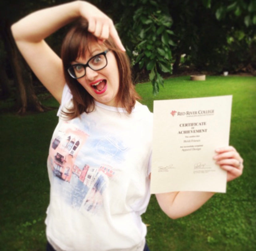 Heidi is wearing a white tshirt, holding a Red River College Certificate of Completion for Apparel Design