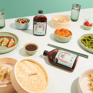 Table with various dishes, including bottles of sauce, bowls of food, and a pair of chopsticks.