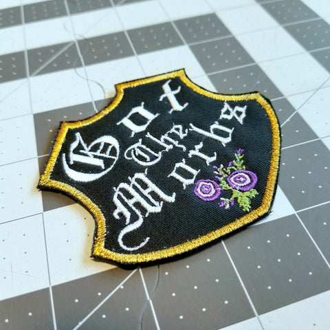 Black emblem-shaped embroidered goth patch with gold border, purple flowers, and the words got the morbs in old English lettering.