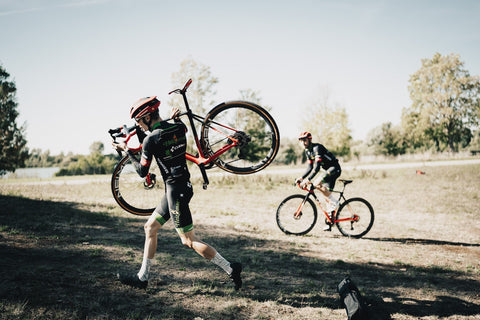 Cyclocross Fahrer trägt sein Bike durch Landschaft