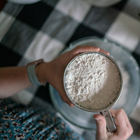 Flour in a sieve, you can still see the hands holding the sieve