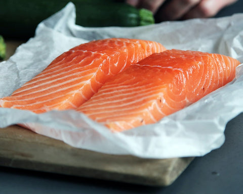 Two salmon fillets on paper on a wooden cutting board