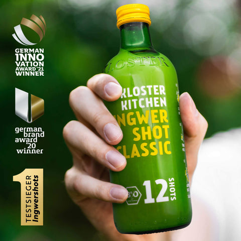 Es wird eine Flasche Ingwer Shot Classic von Kloster Kitchen in die Kamera gehalten. Das Gewinner Logo des German Innovation Awards ist daneben zu sehen. 