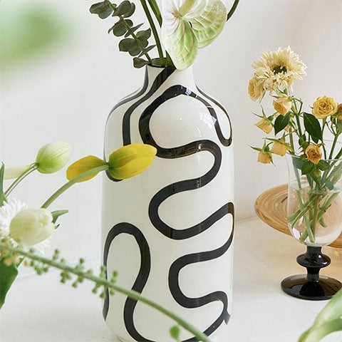 Vase blanc lignes abstraites noires design mise en scène avec des fleurs et des ornements