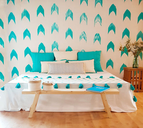 türkis weiße Wandtapete mit großen Bett davor auf dem weiße und türkisfarbende Kissen liegen sowie ein weiß türkisfarbende Tagesdecke  