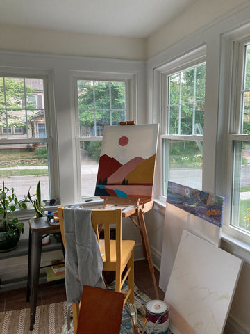 Ashley Miller's workspace, featuring a painting of a desert sunset on an easel