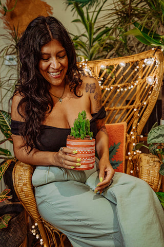Marla posing in a chair surrounded by plants, with a cactus she potted.