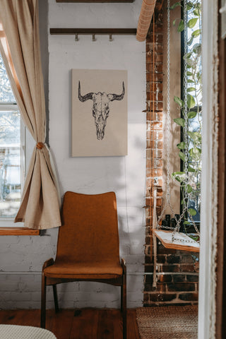 Bull Skull, Vintage Southwestern - Canvas Print Wall Art Décor featuring a detailed bull skull design. Hung above a chair in a bedroom.