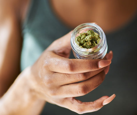 woman holding glass jar of trimmed cannabis flower