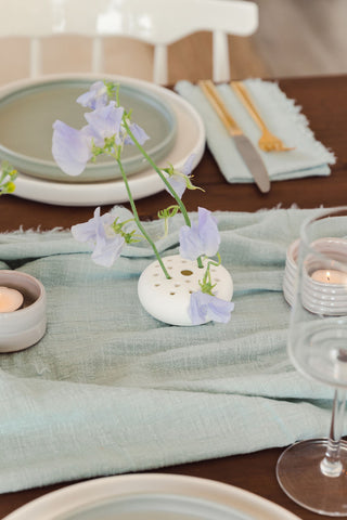 A single flower lays on a light blue linen, a beautiful snapshot of the table decorations provided by Bluum Maison.