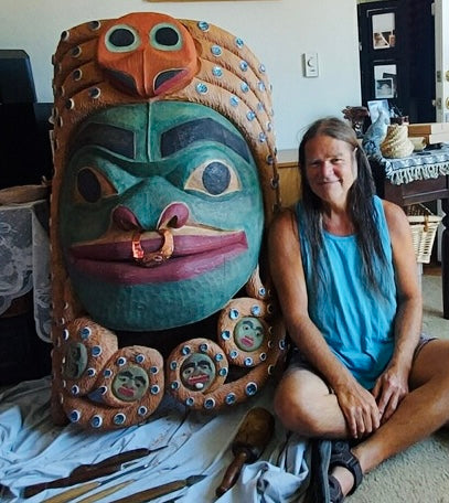 Fred Fulmer Tlingit Artist sitting next to the finished product of the Chookaneidee Devilfish carved cedar giant mask