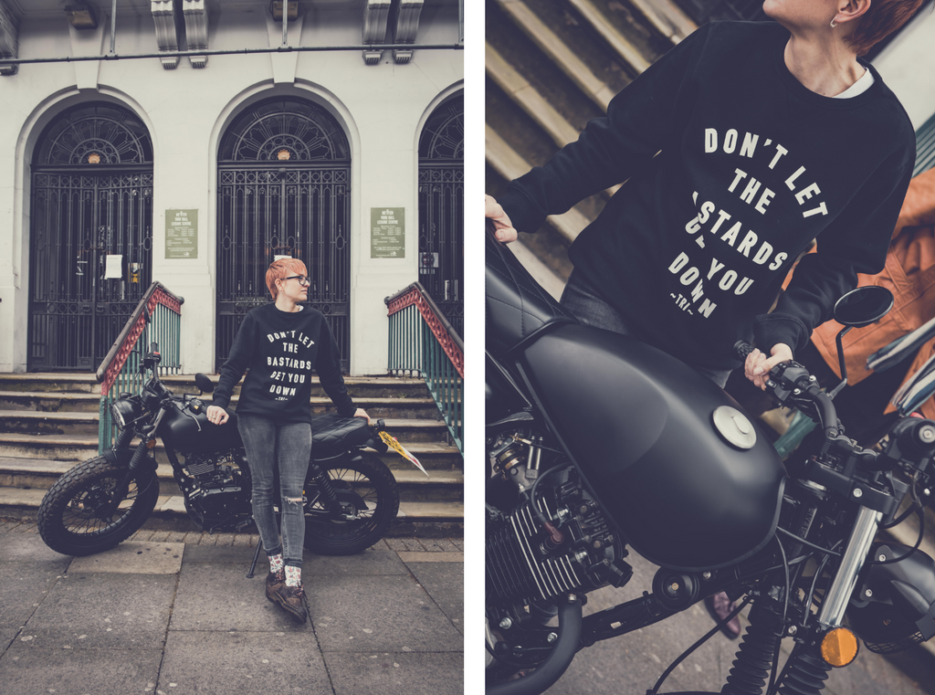 Lady with short orange hair posing infront of a motorbike outside a building with stairs at the store from