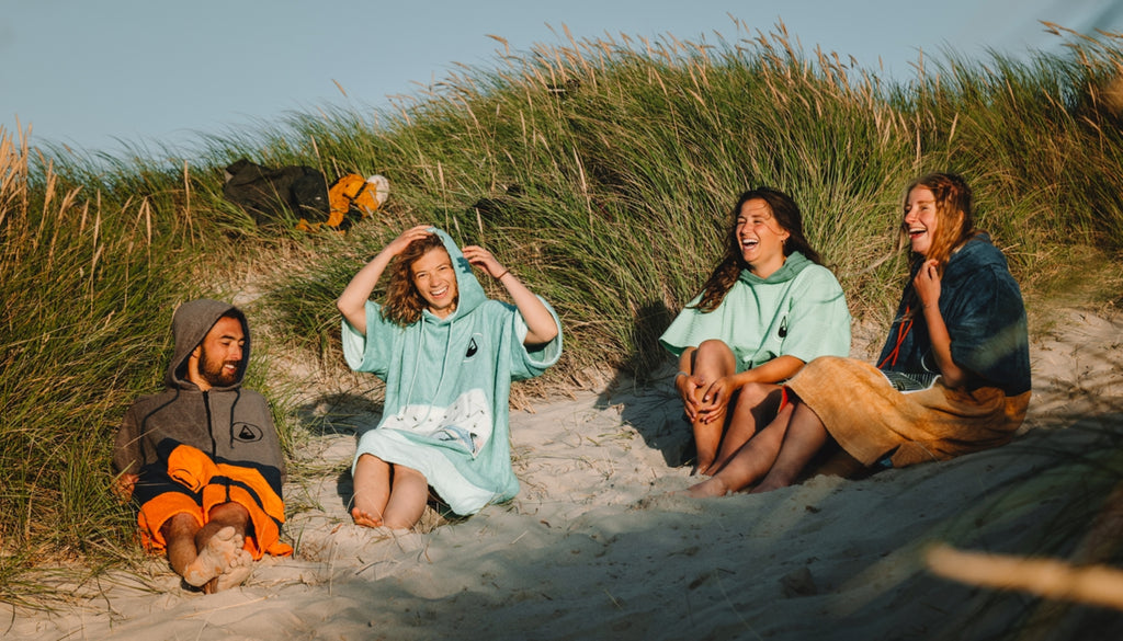 4 Freunde sitzen mit ihren Ponchos im Sand in der Düne.