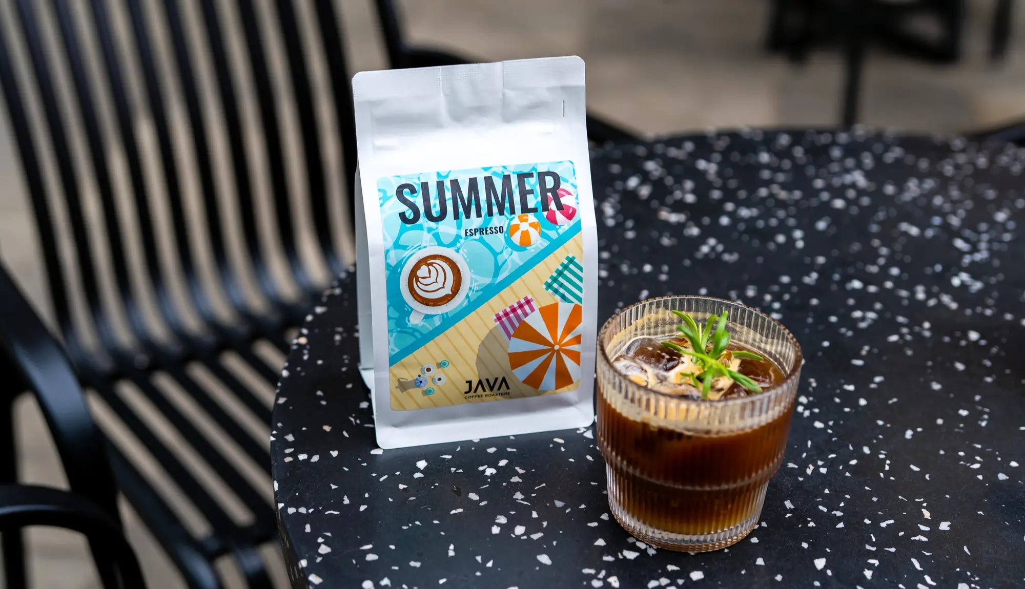 Kawa Java Summer Espresso w letniej oprawie graficznej na stoliku z kawowym drinkiem z lodem i rozmarynem – idealna na chłodne i orzeźwiające espresso latem.