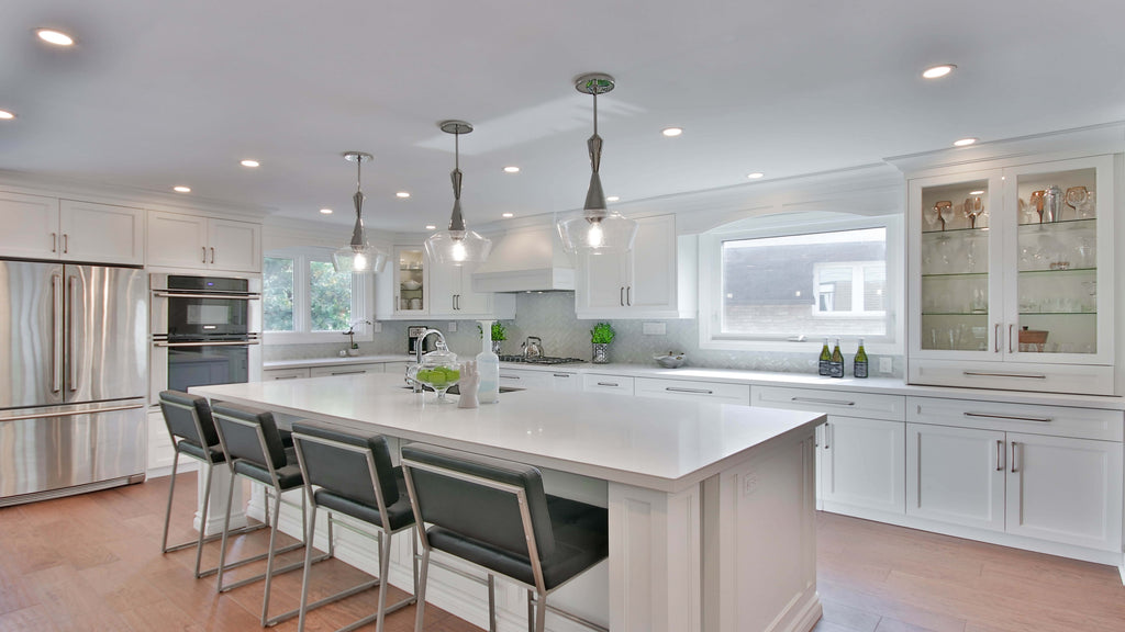 Open shot of white modern kitchen with recessed downlight installed in ceiling and pendant lights with glass bulbs hanging over kitchen island.