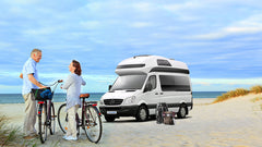 Mercedes Sprinter on a beach by the sea, picnic basket, rucksack and happy couple with bicycles