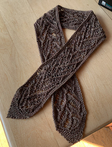 a brown Versailles Scarf laid out on a wooden surface