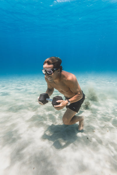 Kai Lenny walks underwater, smile on his face, with a Tru Grit 30lb dumbbell