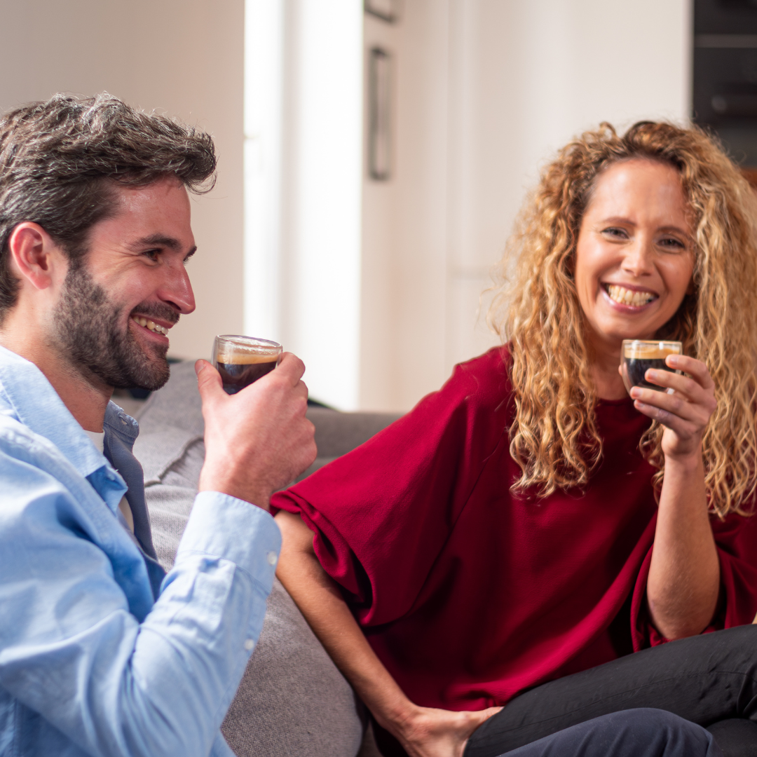 A smiling man and woman enjoying coffee together on a couch.