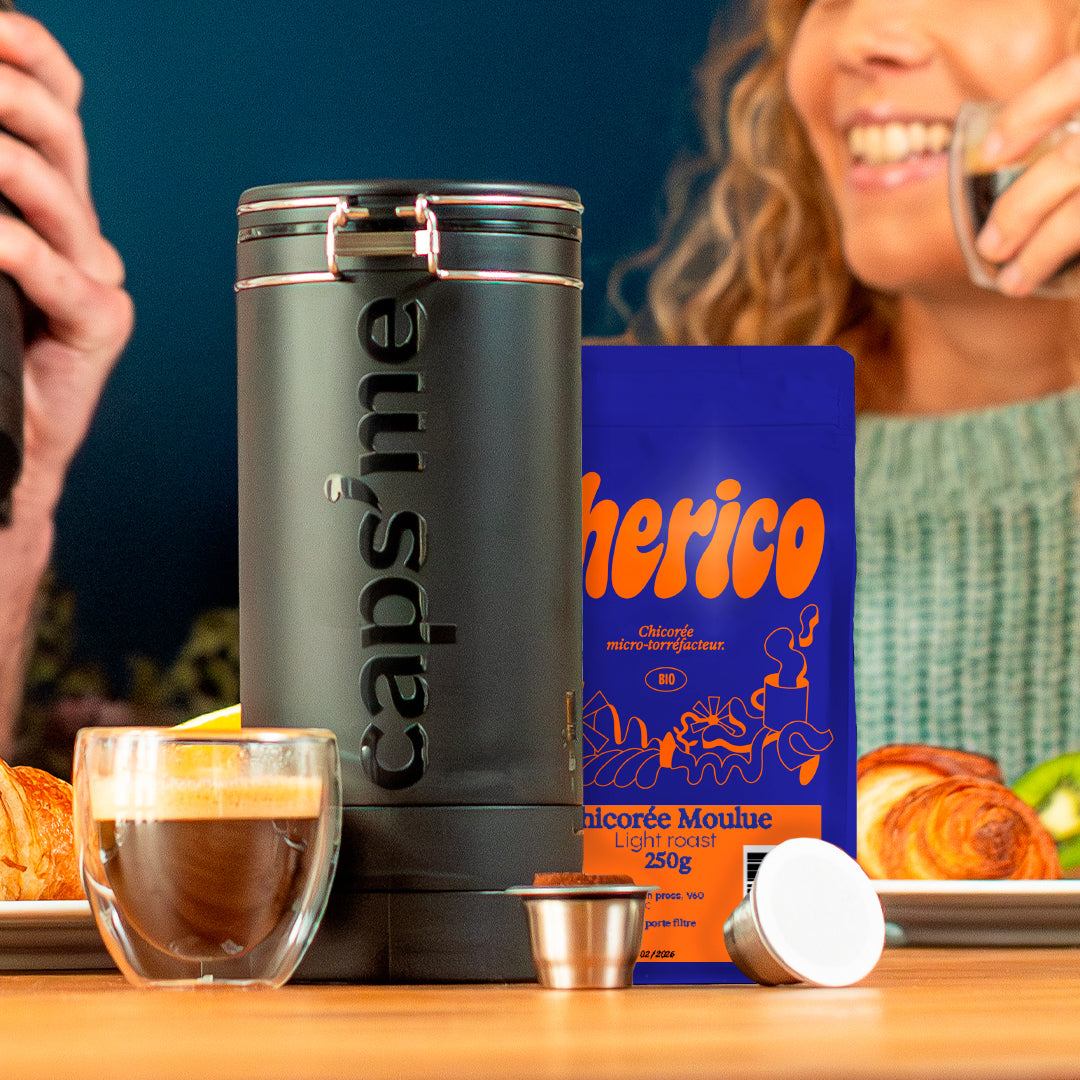 A reusable coffee capsule beside a coffee cup with a smiling woman in the background.