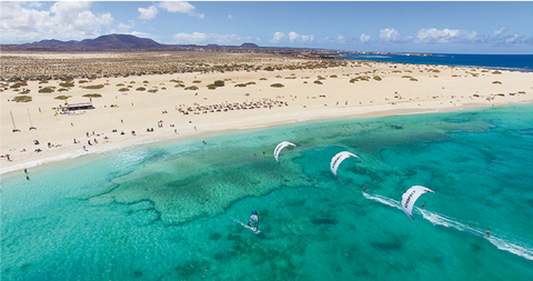 This image shows a beach on Fuerteventura called flag beach, where many kitesurfers are on the water. 