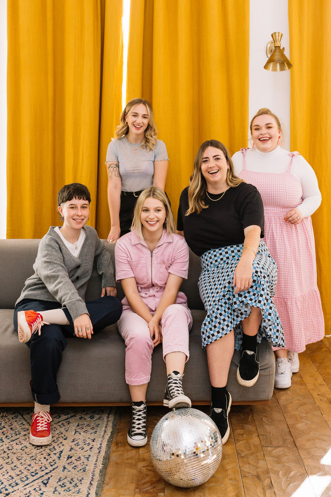 The Weekend IN team sitting together on a sofa in Bristol in front of mustard yellow curtains